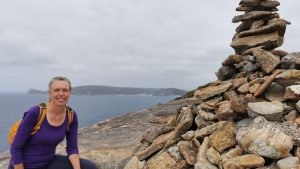Woman hiking beside a pile of rocks with the ocean in the background, symbolizing the journey of healers navigating burnout and finding grounding amidst emotional weight.