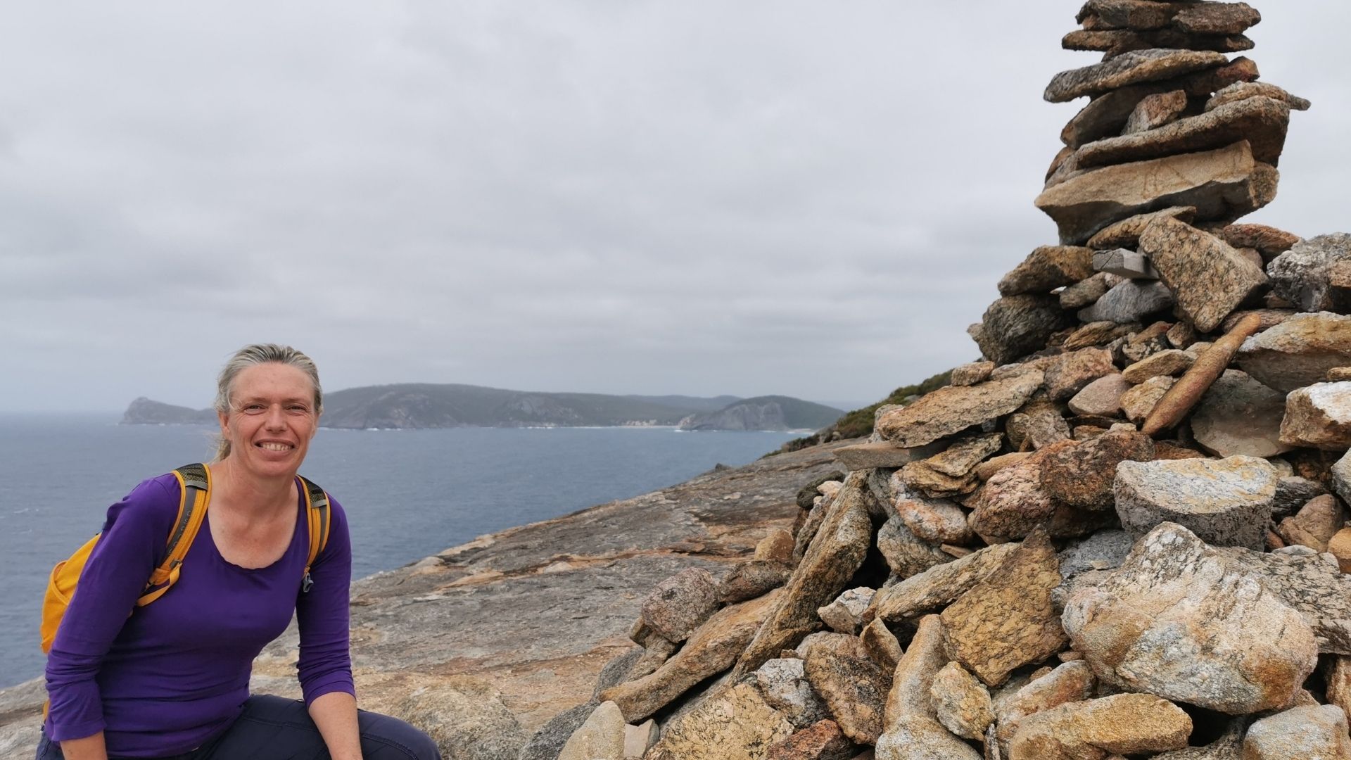 Burnout for healers: when you love your work but it’s too much Woman hiking beside a pile of rocks with the ocean in the background, symbolizing the journey of healers navigating burnout and finding grounding amidst emotional weight.