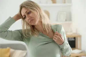 Woman sitting on a couch looking overheated and exhausted, representing the discomfort of hot flashes during menopause.