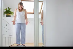 Woman standing on a scale looking puzzled and frustrated, symbolizing the emotional and physical challenge of menopause-related weight gain.
